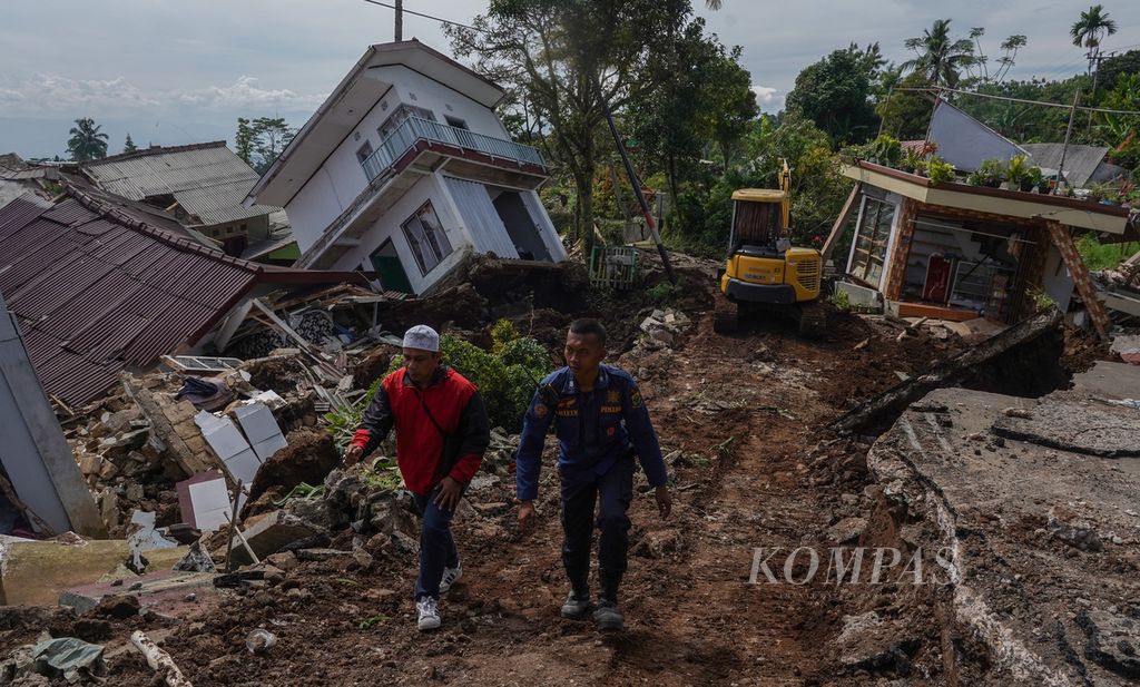 Two SAR members crossing Jalan Cisarua, Sarampad, Cugenang, Cianjur Regency, West Java, against the background of houses that were badly damaged by the earthquake, Wednesday (23/11/2022).
