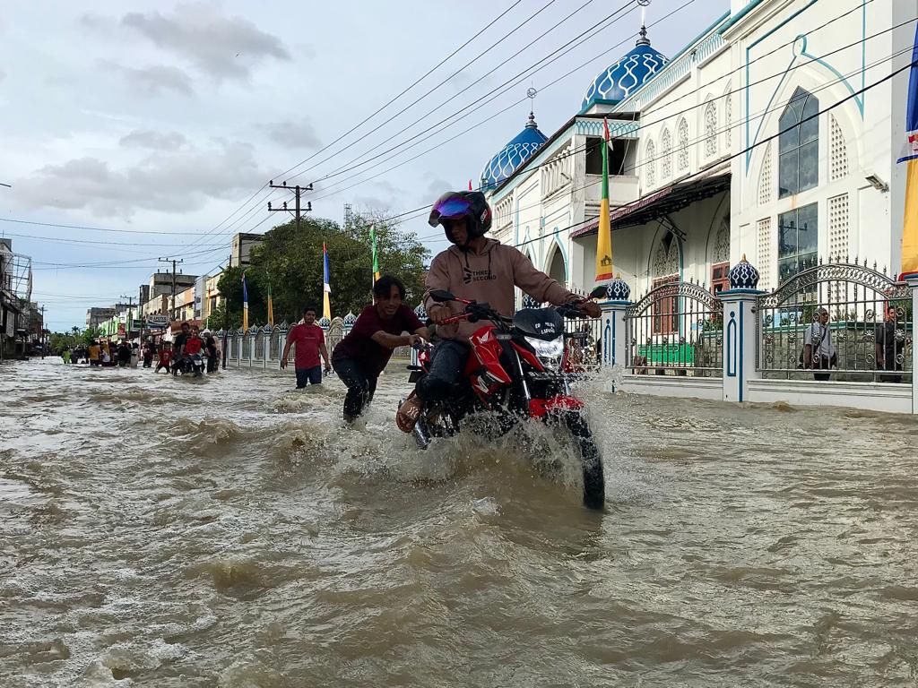 Warga melintasi jalan nasional di Kota Lhoksukon, Kabupaten Aceh Utara, Provinsi Aceh, Sabtu (8/10/2022), yang digenangi banjir. Banjir di Aceh Utara setidaknya menggenangi 142 desa di 14 kecamatan. 