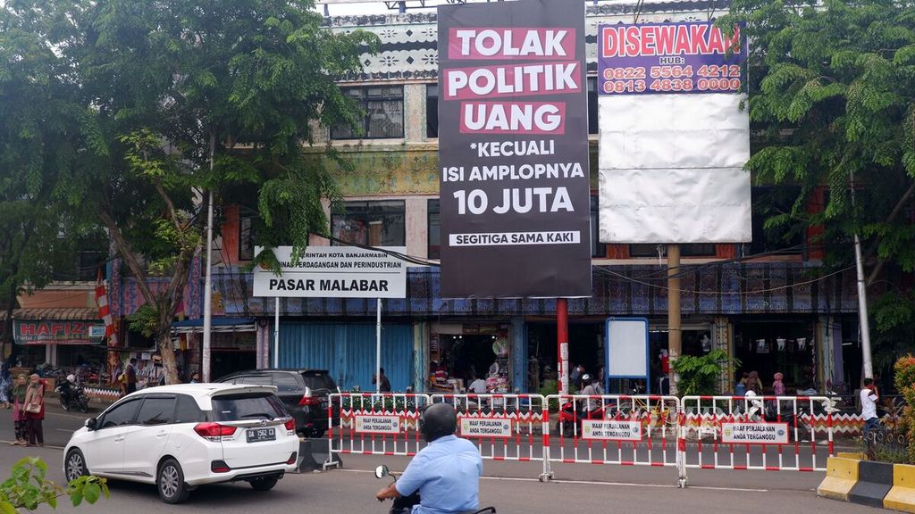Baliho ajakan untuk menolak politik uang bernada satire terpasang di sudut salah satu pasar di Kota Banjarmasin, Kalimantan Selatan, sehari menjelang pemungutan suara pemilihan kepala daerah serentak 2020, Selasa (8/12/2020). Pada 9 Desember 2020, warga Banjarmasin akan memilih gubernur dan wali kota periode 2021-2024.