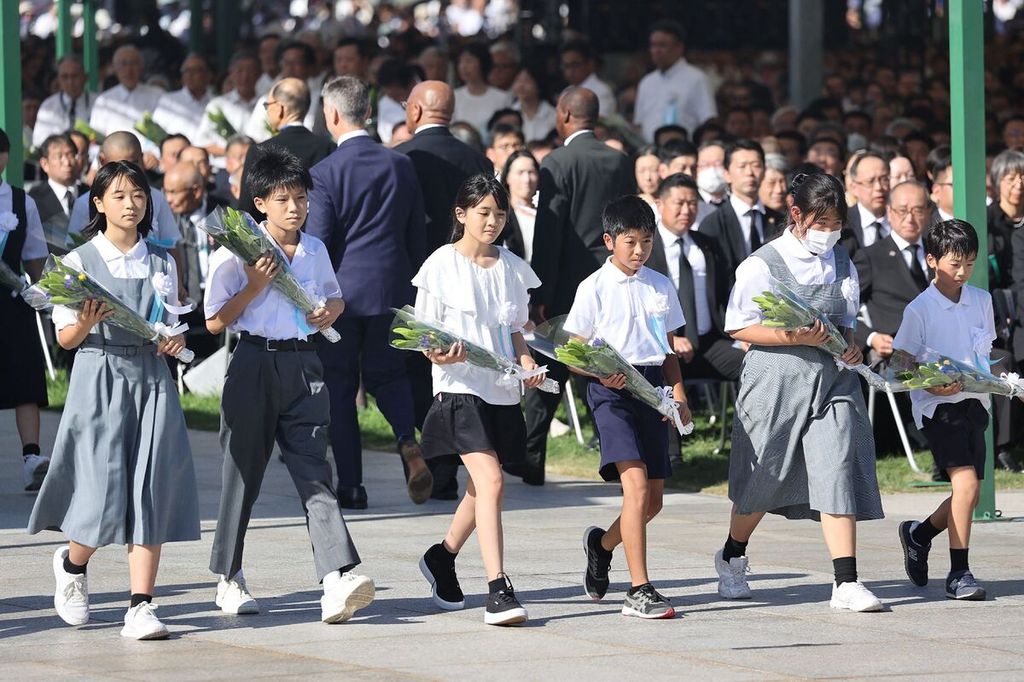 Sejumlah pelajar di Taman Peringatan Perdamaian, Hiroshima, Jepang, Minggu (6/8/2023), berjalan membawa karangan bunga pada upacara peringatan 78 tahun serangan bom atom pertama di dunia. 