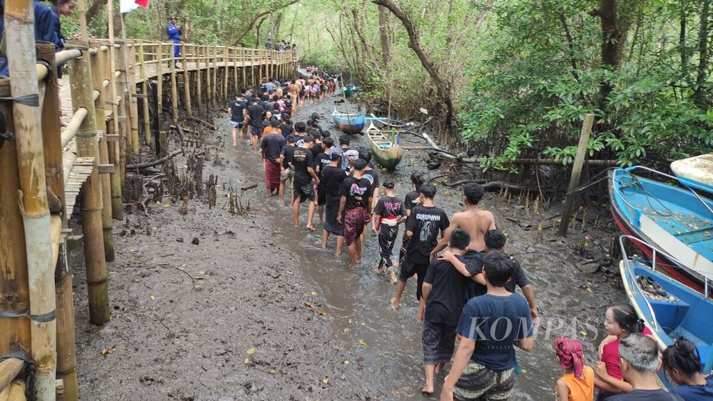<i>Krama </i>(warga) dan <i>yowana </i>(pemuda dan pemudi) Desa Adat Kedonganan, Kedonganan, Kuta, Kabupaten Badung, menyusuri sungai di tengah hutan bakau untuk mengikuti tradisi <i>mabuug-buugan </i>di tengah Taman Hutan Raya Ngurah Rai, Kamis (23/3/2023).