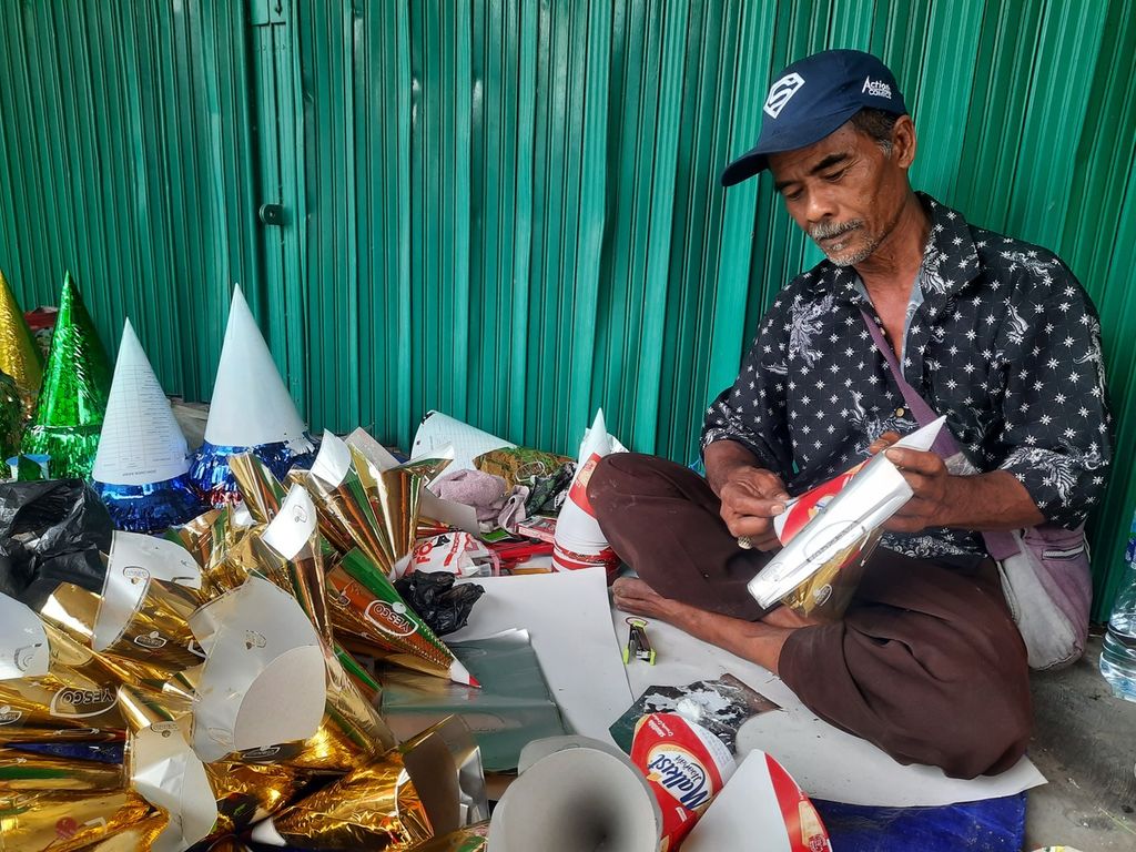 Korsan (60) melekatkan kertas warna pada kerucut terompet yang dibuatnya di Jalan Pintu Besar Selatan, Kota Tua, Jakarta, Sabtu (31/12/2022). Ia datang bersama rekannya, Rojali (50), dari Cikarang, Jawa Barat.