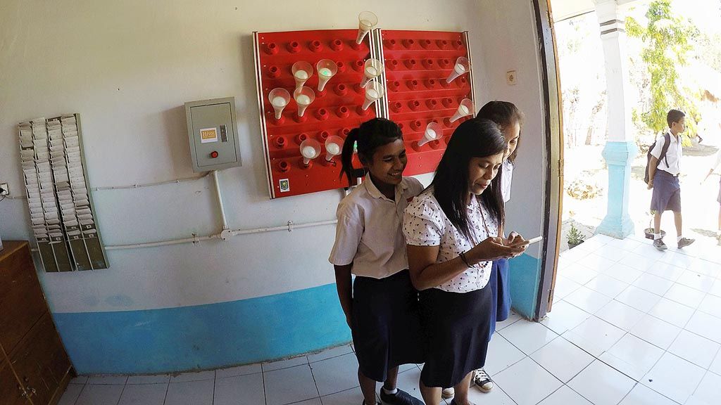 Agustine Alfonite Lay (tengah), guru SMP Negeri Satu Atap di Desa Kataka, Kecamatan Kahaungu Eti, Kabupaten Sumba Timur, Nusa Tenggara Timur,  memeriksa telepon seluler miliknya bersama dua muridnya, Rabu (13/9).