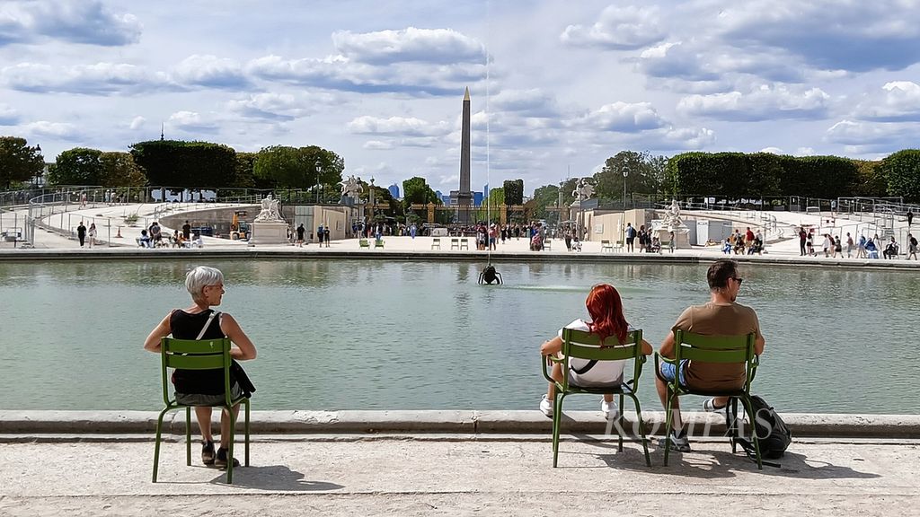 Wisatawan sedang duduk di Jardin des Tuileries (Taman Tuileries) sambil menghadap kolam dan Obélisques de Louxor (tugu Obelisk Mesir kuno), Paris, Perancis, Kamis (20/7/2023).