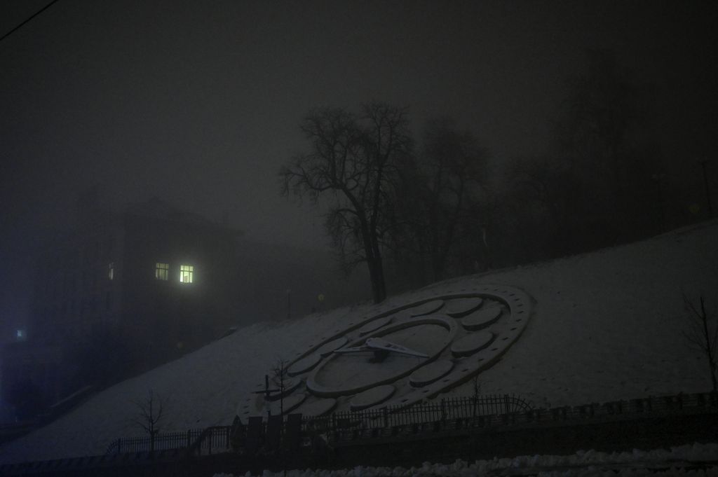 Foto yang diambil pada 24 November 2022 ini menunjukkan Jam Bunga yang tertutup salju dan cahaya dari sebuah jendela di malam berkabut di Kyiv, Ukraina, di tengah invasi Rusia. 