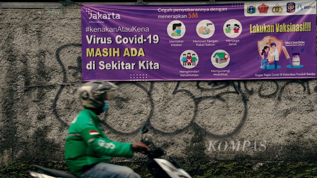 Pengendara sepeda motor melintasi spanduk kampanye untuk tetap menjaga protokol kesehatan di Pondok Bambu, Jakarta Timur, Rabu (16/2/2022). 