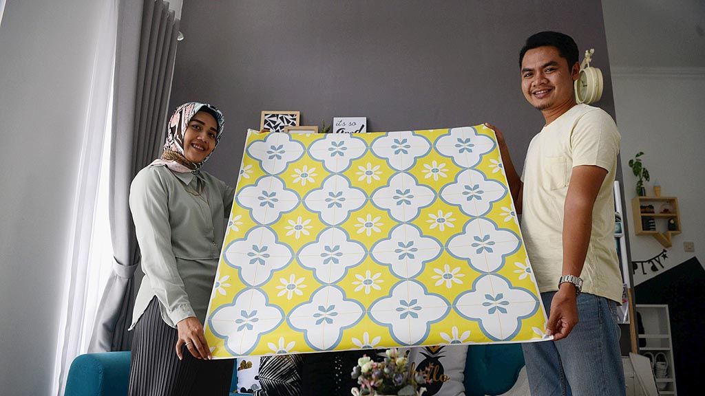 Ariyuni Trikada Putri (29) dan Gunarto Budi Handoyo (30) membentangkan stiker lantai  di rumah mereka di kawasan Kecamatan Bangunjiwo, Kasihan, Bantul, Kamis (27/4). Contoh stiker lantai motif tegel dari Riz Studio.