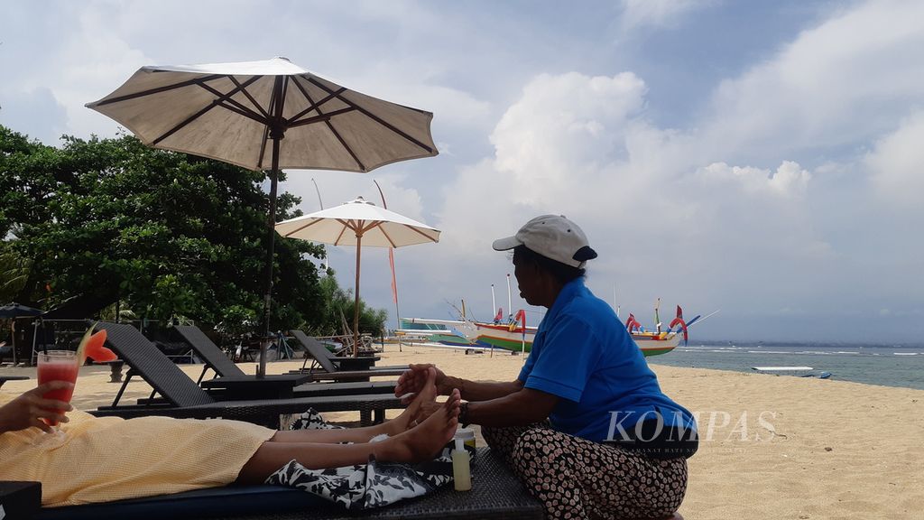 Amy (60), melayani pelanggan refleksi saat berwisata di Pantai Sindhu, Sanur, Bali, Sabtu (13/11/2022).