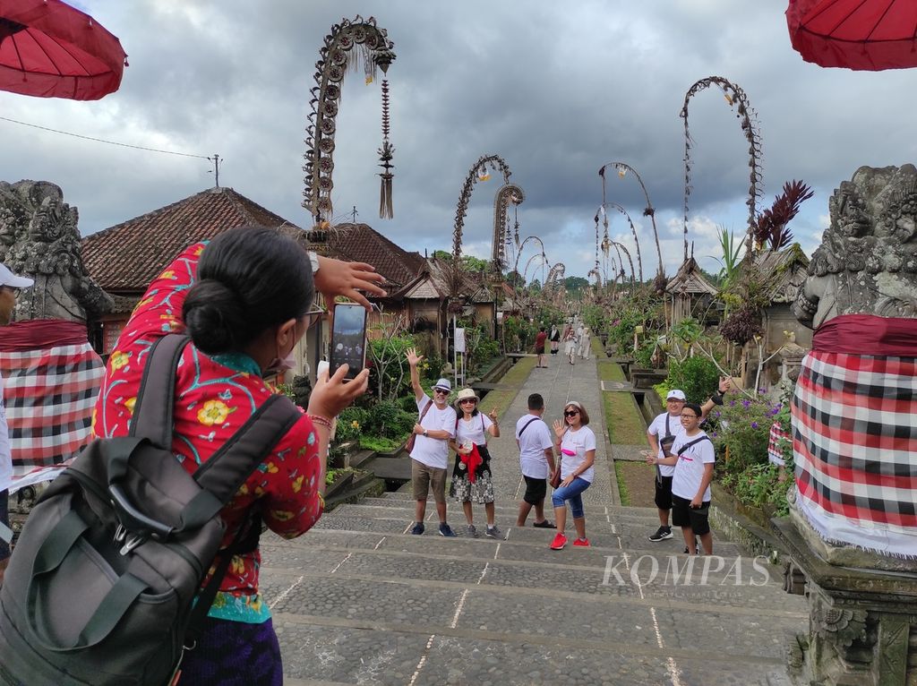 Seorang pemandu wisata tengah memfoto kelompok wisatawan lokal dengan latar lanskap Desa Adat Penglipuran, Kabupaten Bangli, Bali, Selasa (28/6/2022). 