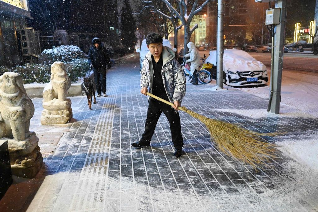 Seorang warga Beijing tengah membersihkan trotoar dari tumpukan salju di depan sebuah rumah makan, Kamis (14/12/2023).