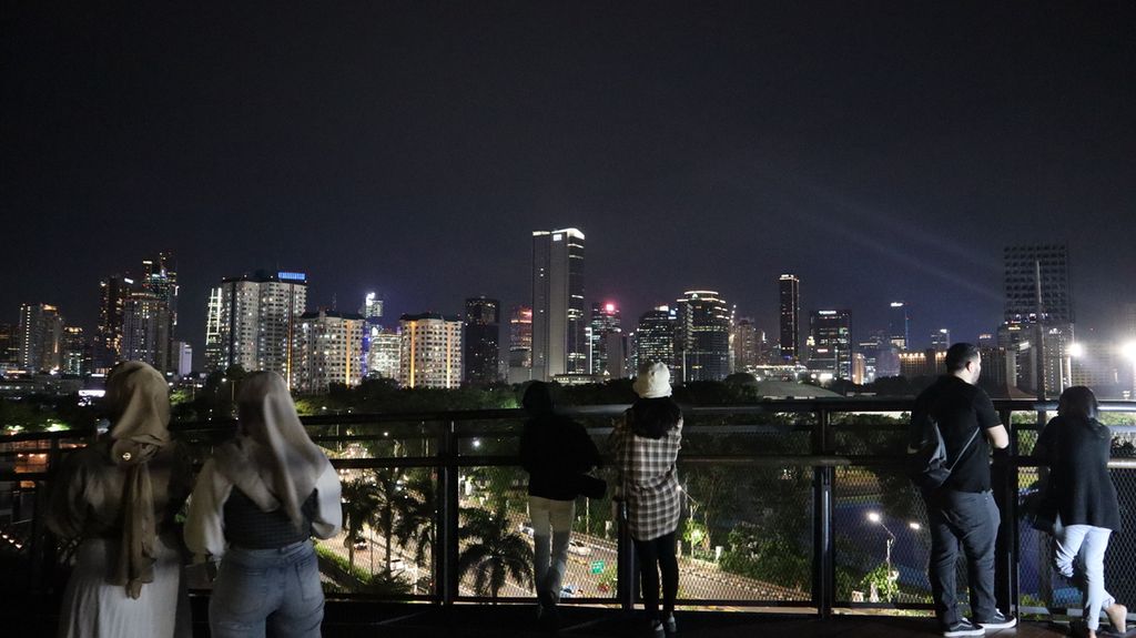 Warga menikmati pemandangan kota Jakarta pada malam hari dari jembatan Skywalk di atap gedung Mal Senayan Park, Jakarta Pusat, Rabu (8/2/2023).