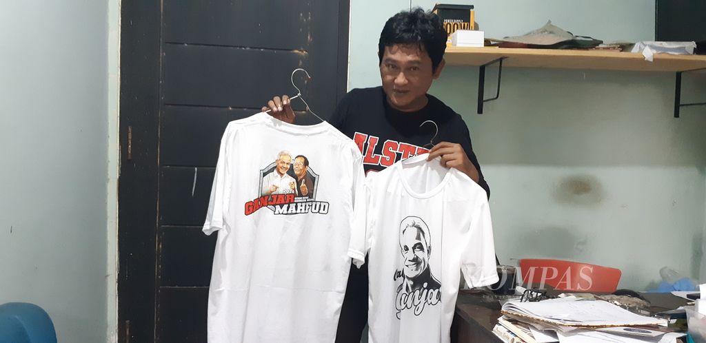 Hendri menunjukkan contoh produk kaus Pemilu 2024 bergambar calon presiden dan wakil presiden di Sidoarjo, Jatim, Rabu (6/12/2023). Pesanan kaus pemilu meningkat, tetapi tidak seramai pada Pemilu 2019. 