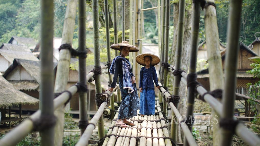 Ana (kiri) dan Mila menunggu rekannya melewati jembatan bambu di Kampung Gajeboh, Desa Kanekes, Kecamatan Leuwidamar, Kabupaten Lebak, Banten, Kamis (16/3/2023). Hubungan sosial masyarakat bisa terjaga melalui bahasa.