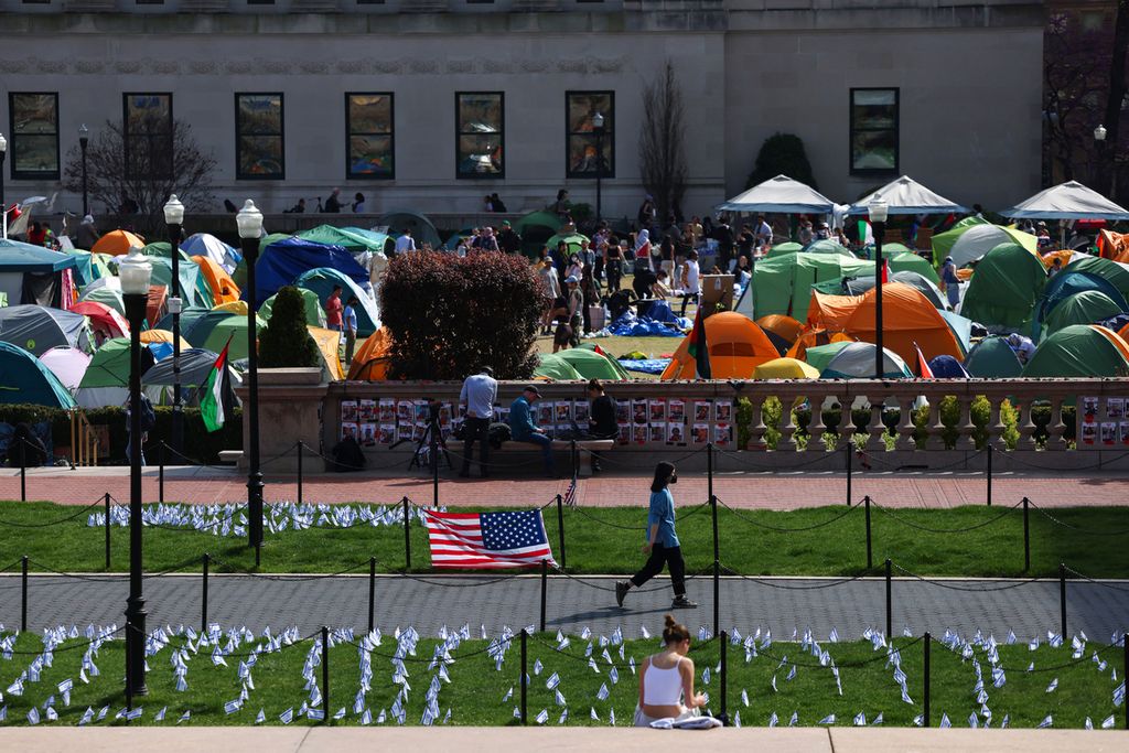 A woman walks past the flag of the United States in front of a pro-Palestine camp at Columbia University in New York City, USA, on Sunday (28/4/2024).