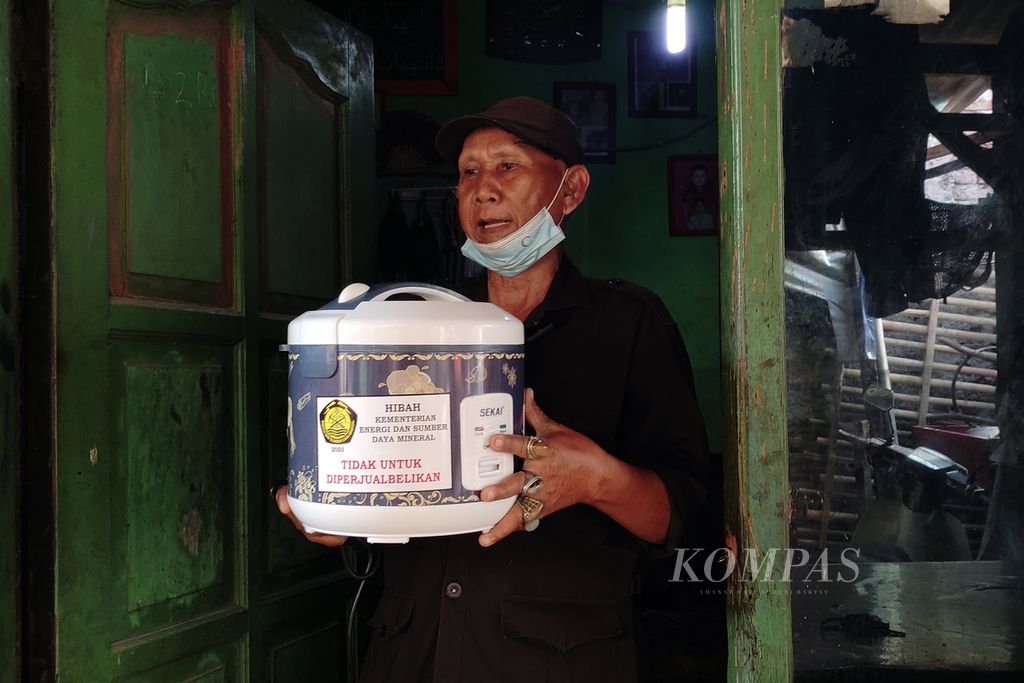 Satiman (63), warga Kelurahan Pulo Gebang, Kecamatan Cakung, Jakarta Timur, menerima alat memasak berbasis listrik (AML)/<i>rice cooker </i>dari Kementerian Energi dan Sumber Daya Mineral (ESDM), Selasa (12/12/2023). 