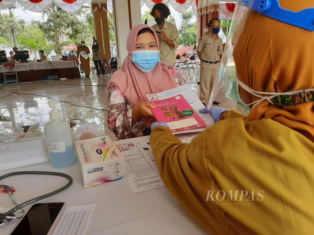Seorang tenaga medis mengecek buku kesehatan ibu dan anak dan menyerahkannya kepada ibu hamil, sesaat sebelum ibu tersebut menjalani vaksinasi, Senin (30/8/2021).