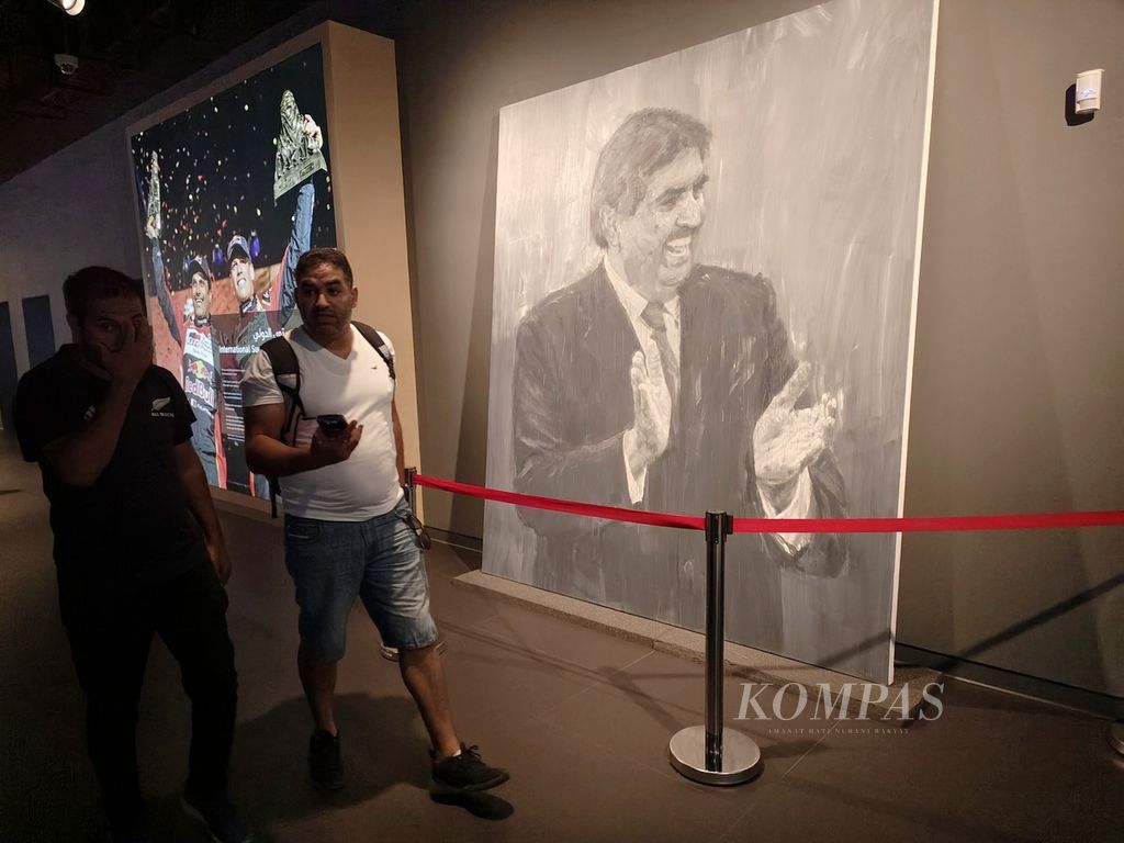 Dua pengunjung melintas di depan lukisan raksasa ayah Amir Qatar, Sheikh Hamad bin Khalifa Al-Thani, yang berada di 3-2-1 Museum Olahraga dan Olimpiade Qatar (QOSM) di kompleks Stadion Internasional Khalifia, Doha, Rabu (30/11/2022). Museum itu menampilkan berbagai sejarah perkembangan olahraga di Qatar.