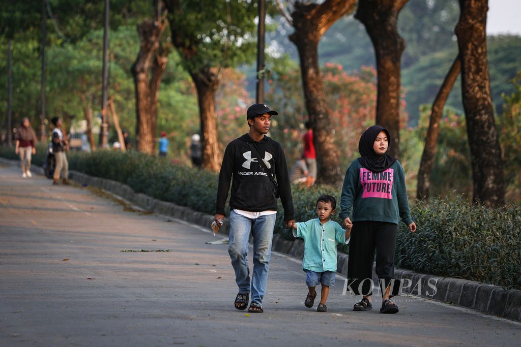 Satu keluarga berjalan-jalan di tepi aliran Kanal Banjir Timur di kawasan Duren Sawit, Jakarta Timur, Sabtu (16/12/2023). 
