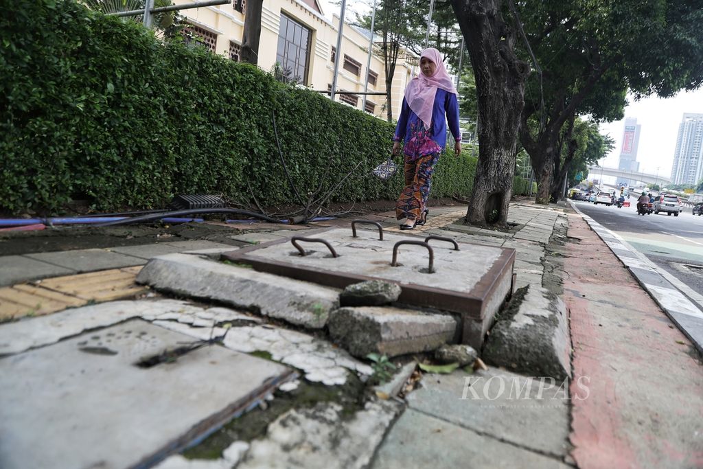 Pejalan kaki melintasi trotoar yang tidak rata di Jalan Gatot Subroto, Jakarta, Jumat (1/3/2024). Meski proyek revitalisasi trotoar terus digiatkan, kondisi trotoar di sejumlah wilayah di Jakarta masih menyulitkan pejalan kaki untuk melintas. 