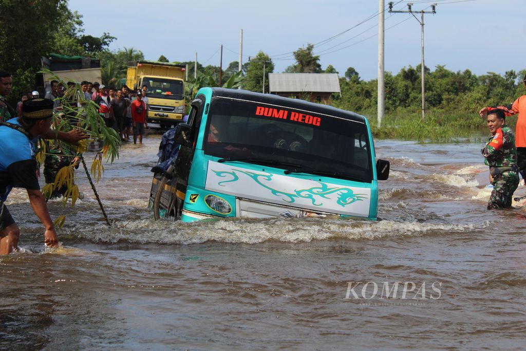 Residents of Lembeng Village, South Hamlet District, South Barito Regency, Central Kalimantan, on Thursday (25/1/2024), helped a pickup truck passing through a flood spot on the Trans-Kalimantan route. Several trucks and cars that forced their way through were pushed due to engine failure when they were submerged in water.