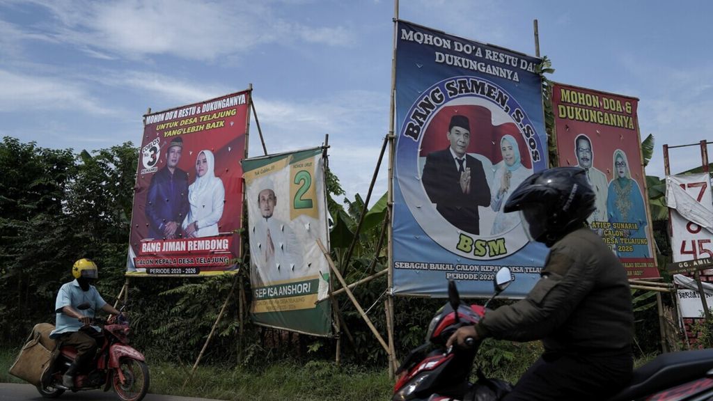 Warga melintas di depan baliho bergambar bakal calon kepala desa Telajung periode 2020-2026 di Kecamatan Cikarang Barat, Kabupaten Bekasi, Jawa Barat, Senin (6/7/2020). 