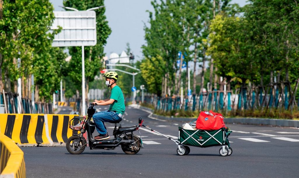 Seorang warga yang mengendarai skuter listrik menarik troli berisi bahan makanan setelah warga mulai diizinkan meninggalkan kompleks mereka selama beberapa jam saat pelonggaran pembatasan Covid-19 diberlakukan di Distrik Pudong, Shanghai, China, Minggu (22/5/2022).