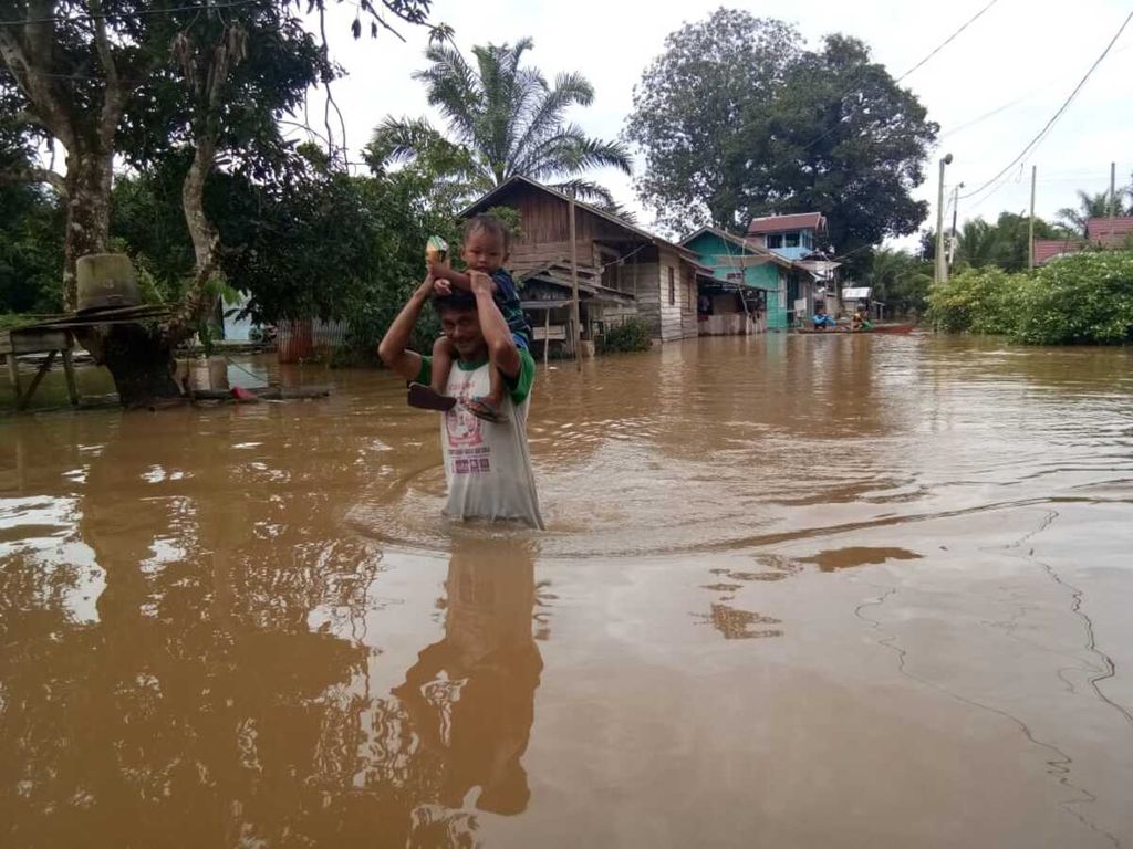 Warga Desa Nanga Mua, Kecamatan Arut Utara, Kabupaten Kotawaringin Barat, Kalimantan Tengah, melintas di tengah banjir yang melanda desanya, Jumat (7/12/2018). 