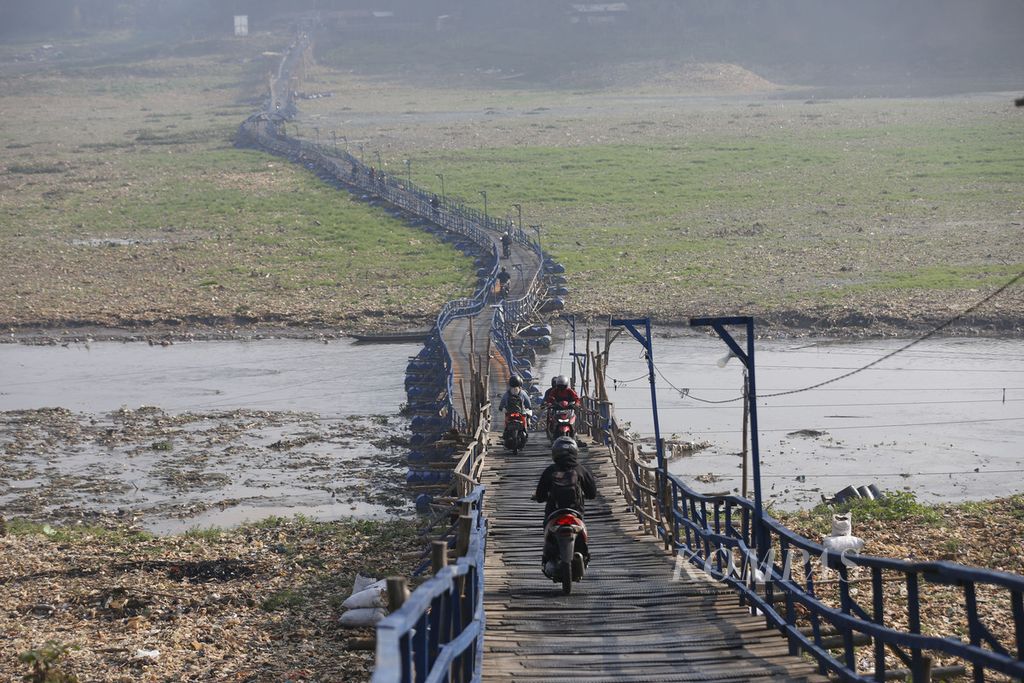 Pengendara sepeda motor melintas di atas sungai yang mengering.