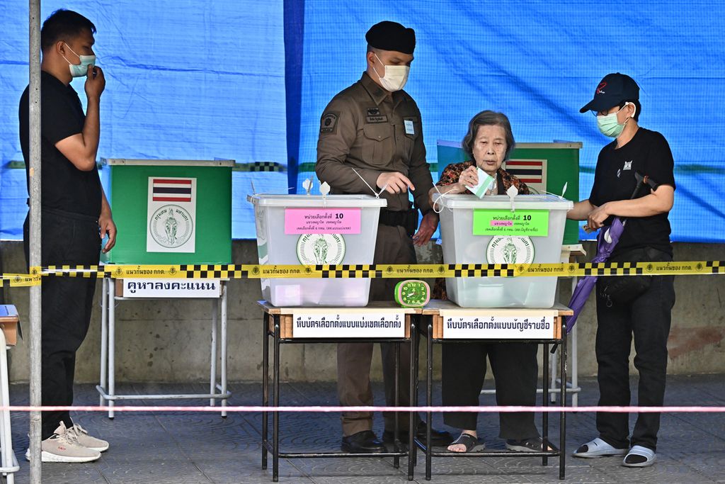 Seorang perempuan lanjut usia dengan diawasi petugas pemungutan suara memasukkan surat suara setelah menggunakan hak piilhnya di sebuah tempat pemungutan suara di Bangkok, Minggu (14/5/2023). Pemilu kali ini dipandang sebagai titik persimpangan bagi politik Thailand, akan bertahan dengan rezim militer yang sudah dua periode berkuasa atau perubahan. 