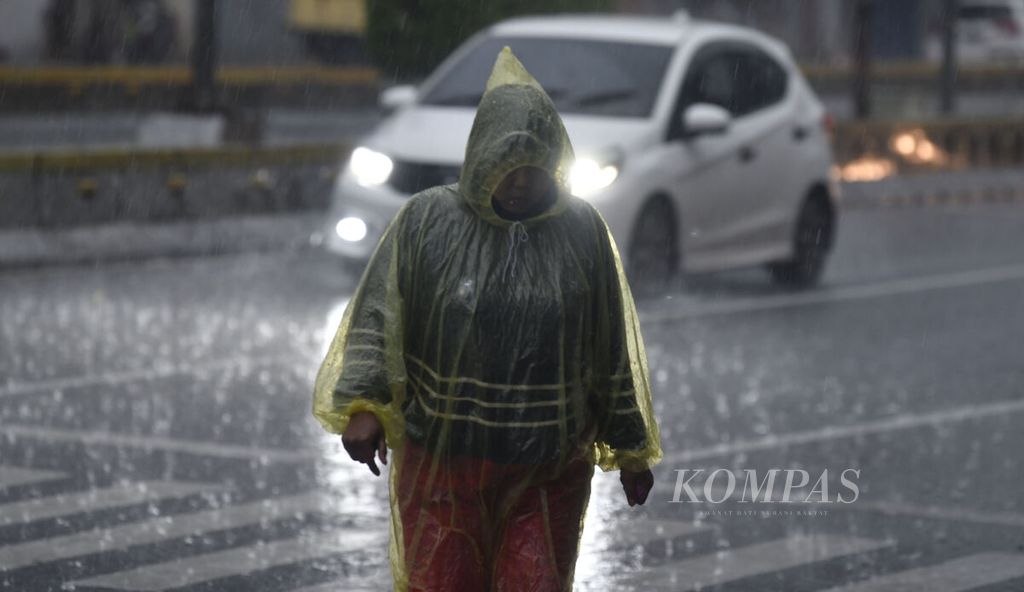 Warga mengenakan mantel berjalan kaki melewati hujan deras di kawasan Petojo, Jakarta Pusat, Selasa (4/10/2022).  