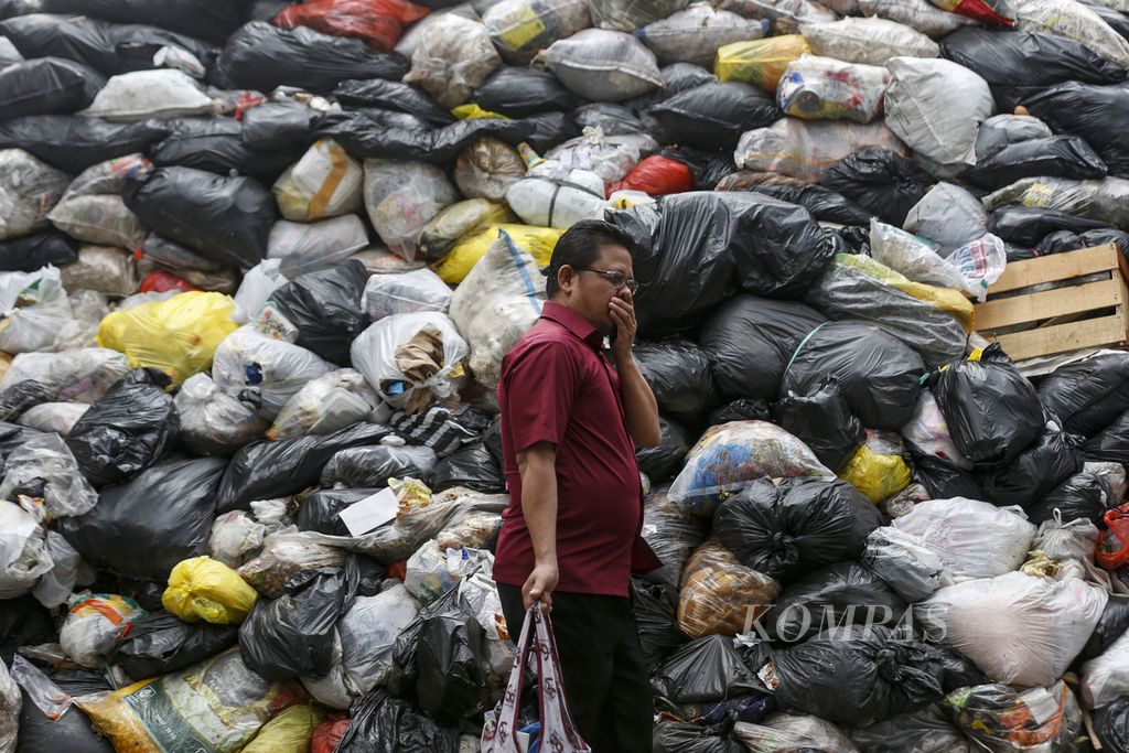 Warga menutup hidungnya saat berjalan di samping tumpukan sampah di tempat pembuangan sementara (TPS) Pasar Gegerkalong, Kota Bandung, Jawa Barat, Rabu (11/10/2023).