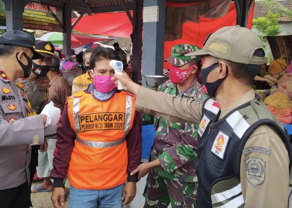 Petugas Satpol PP Kota Makassar mengecek suhu tubuh seorang warga yang terjaring razia protokol kesehatan, Minggu (13/9/2020). Selanjutnya warga akan dikirim mengikuti tes usap tenggorokan.