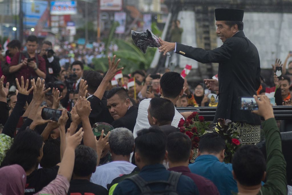 Presiden ketujuh RI Joko Widodo membagikan kaus kepada warga saat melintas di Jalan Colomadu, Karanganyar, Jawa Tengah, Minggu (20/10/2024). Joko Widodo resmi purnatugas dari Presiden Indonesia dan kembali pulang ke Solo. 