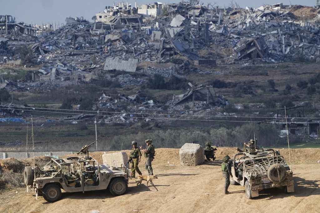 Foto yang diambil pada Jumat (29/12/2023) ini memperlihatkan tentara Israel tengah mengambil posisi tak jauh dari perbatasan Gaza di wilayah Israel bagian selatan. Latar belakang foto ini memperlihatkan Gaza yang hancur oleh serangan bom Israel. 