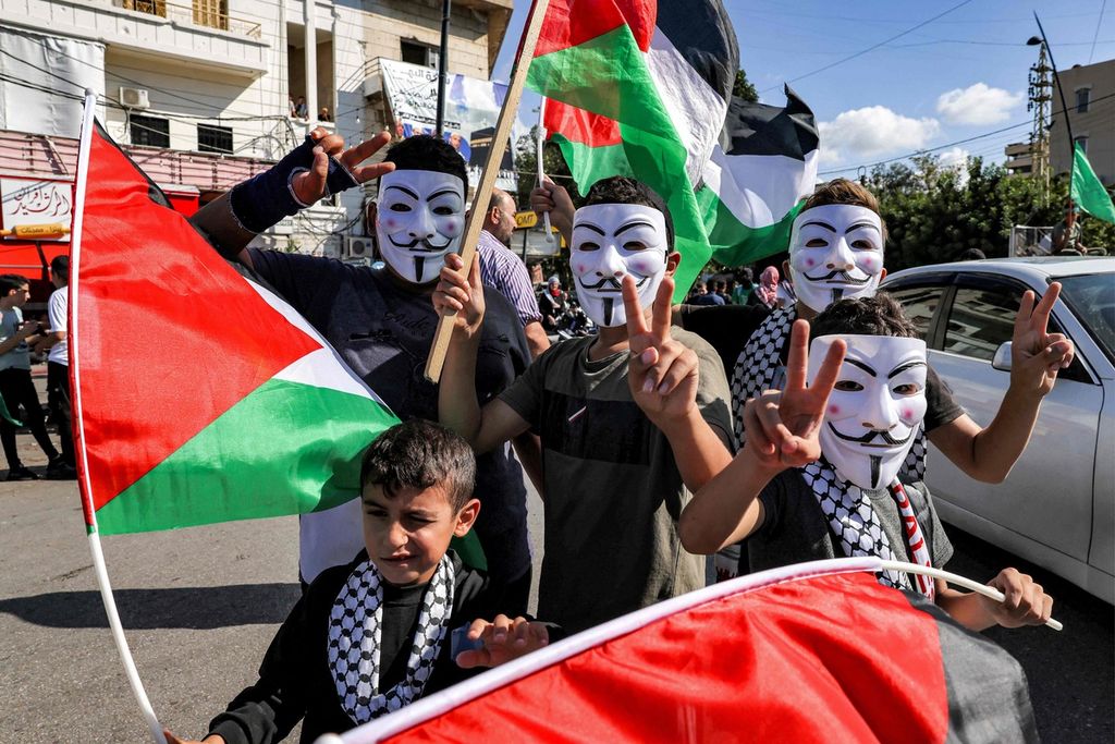 Anak-anak, dengan mengenakan topeng Guy Fawkes, memperlihatkan gestur tanda "kemenangan (<i>victory</i>) dan membawa bendera dalam unjuk rasa mendukung Palestina di Beirut, Lebanon, Jumat (20/10/2023). Perang Hamas-Israel dikhawatirkan bereskalasi menyusul baku tembak artileri dan roket antara Israel dan kelompok Hezbollah di Lebanon selatan. 