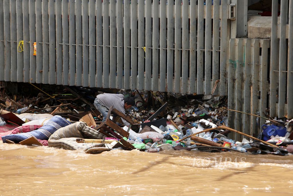Pemulung mencari barang yang masih bisa dimanfaatkan dan bernilai ekonomi di antara sampah yang tersangkut di Pintu Air Manggarai, Jakarta, Kamis (2/1/2020). Berbagai jenis sampah, seperti plastik, ranting pohon, dan sampah rumah tangga, banyak terbawa arus Sungai Ciliwung.
