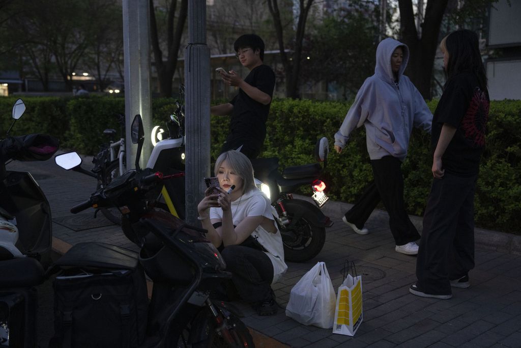 Seorang perempuan menelusuri ponselnya saat menunggu kendaraan yang akan ditumpangi di sebuah ruas jalan di Beijing, China, 16 April 2024. 