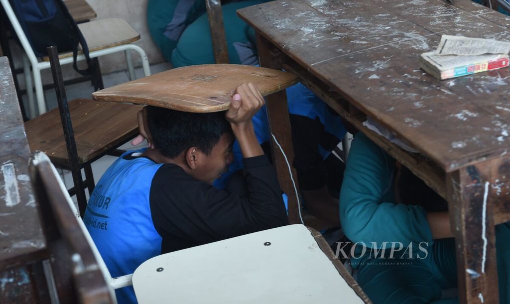 Sambil menutupi kepala dengan papan, Siswa menyelamatkan diri saat simulasi penanganan bencana gempa bumi di SMPN 27 Surabaya, Kota Surabaya, akhir November 2022.