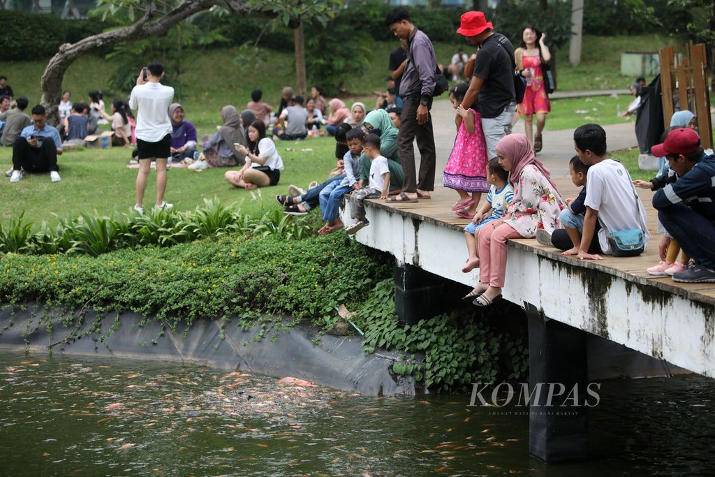 Warga memberi makan ikan di kolam Hutan Kota Gelora Bung Karno, Jakarta, Minggu (25/6/2023).