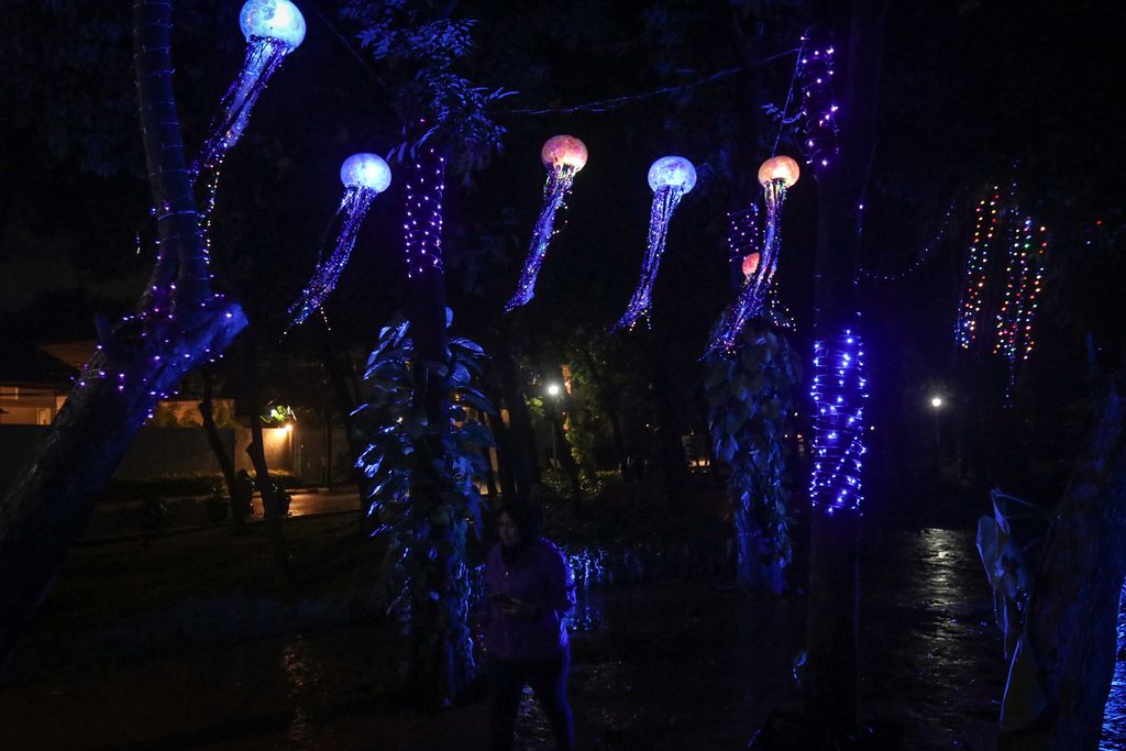 Seorang pengunjung melintas di bawah gemerlap lampu berbentuk ubur-ubur dalam Jakarta Light Festival di Taman Sumenep Promenade, Jakarta Pusat, Senin (26/12/2022). Pemerintah Provinsi DKI Jakarta turut menggelar perayaan Natal dan Tahun Baru di sejumlah lokasi, salah satunya Jakarta Light Festival. Gemerlap cahaya lampu dengan berbagai bentuk yang atraktif menghiasi Taman Sumenep Promenade dari 22 Desember 2022 hingga 5 Januari 2023. 