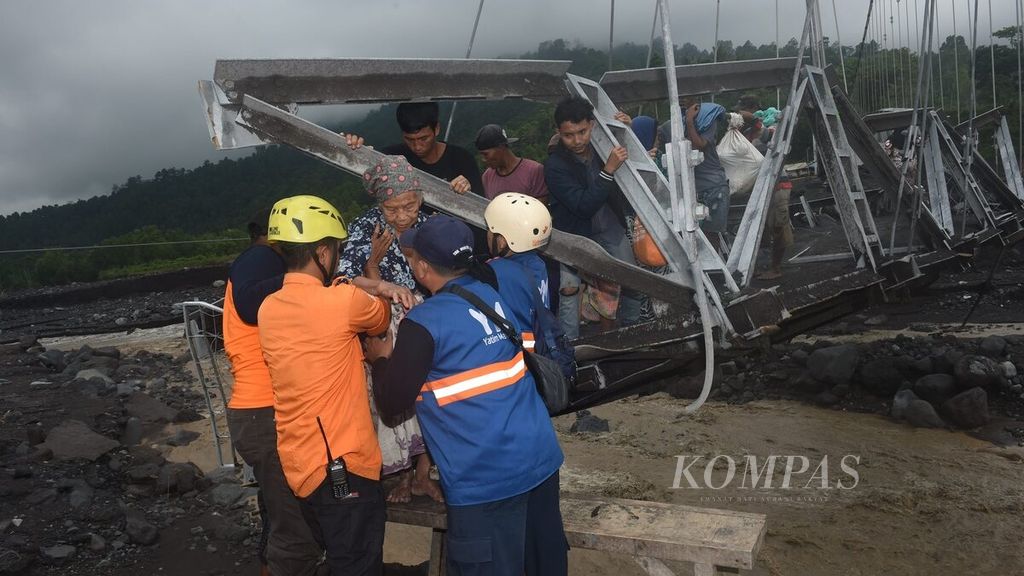 Relawan membantu warga melewati jembatan gantung yang rusak akibat terjangan banjir lahar hujan Gunung Semeru di Dusun Bondeli Selatan, Desa Sumberwuluh, Kecamatan Candipuro, Lumajang, Sabtu (8/7/2023). Akibat cuaca ekstrem pada Jumat (7/7/2023) di Lumajang enam jembatan putus akibat banjir limpasan lahar hujan Gunung Semeru. Satu jembatan merupakan akses penting yang menghubungkan Kabupaten Lumajang dengan Kabupaten Malang. Banjir juga menyebabkan 571 warga mengungsi di 13 titik. BMKG kelas I Juanda Sidoarjo merilis cuaca ekstrem berpotensi terjadi di sejumlah wilayah Jawa Timur pada 7-13 Juli 2023.