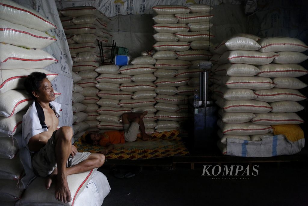 Buruh beristirahat di antara tumpukan karung beras di Pasar Induk Beras Cipinang, Jakarta, Minggu, (12/11/2023). 