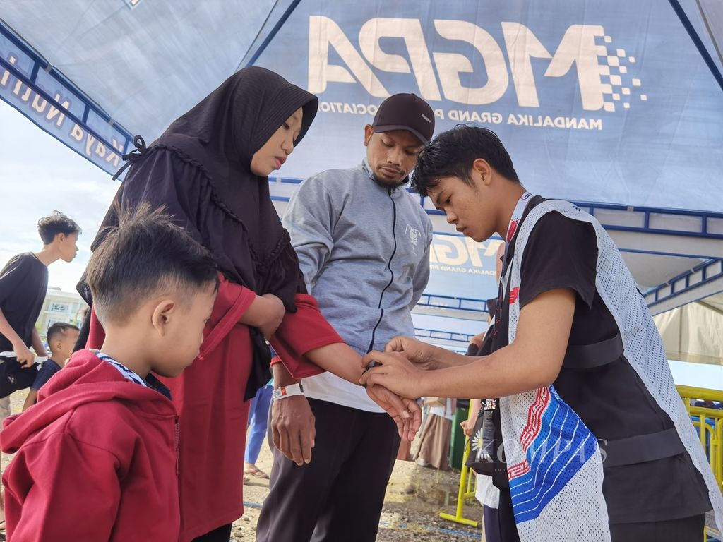 Petugas membantu penonton memasang gelang tiket sebelum masuk ke tribune menyaksikan balapan pada hari ketiga Kejuaraan Dunia Superbike atau WSBK Mandalika, Nusa Tenggara Barat, Minggu (5/3/2023).