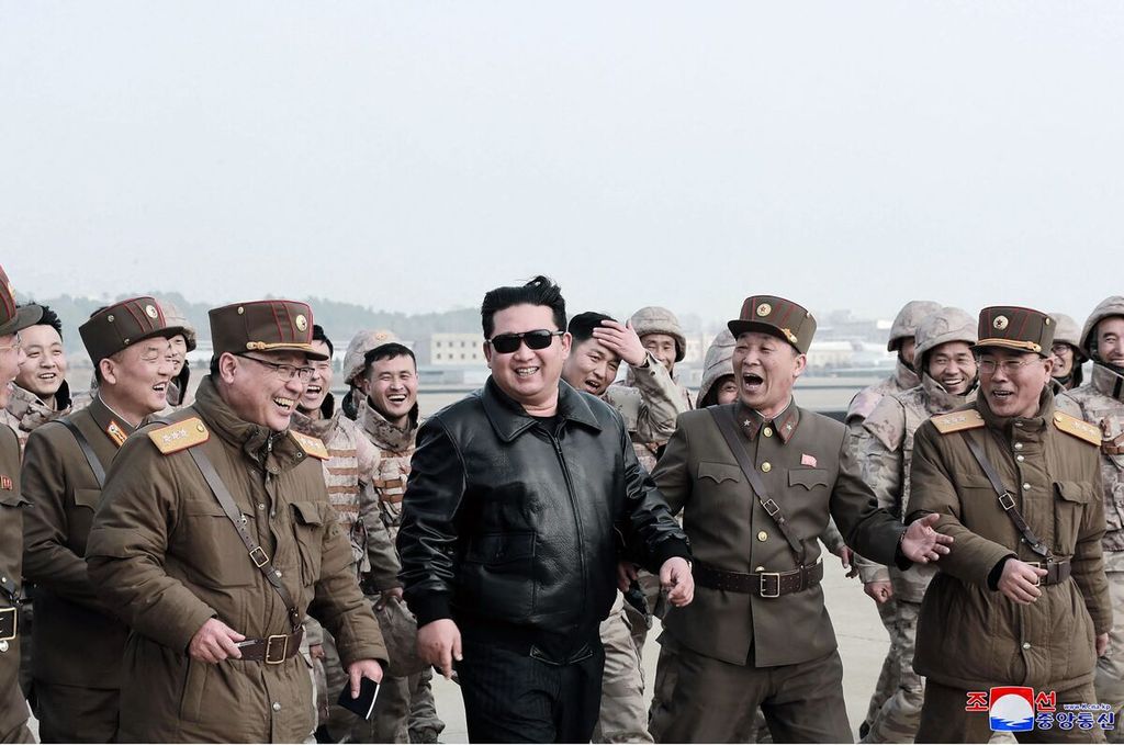 Pemimpin Korea Utara Kim Jong Un (tengah) tertawa bersama personel militer negaranya dalam peluncuran rudal balistik antarbenua, Hwasong-17, di lokasi yang tak disebutkan pada 24 Maret 2022. 