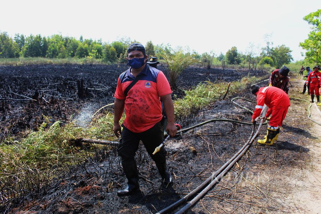 Petugas pemadam kebakaran hutan dan lahan melakukan pembasahan lahan yang baru saja terbakar di Jalan Kalibata, Kota Palangkaraya, Kalimantan Tengah, Senin (14/8/2023).