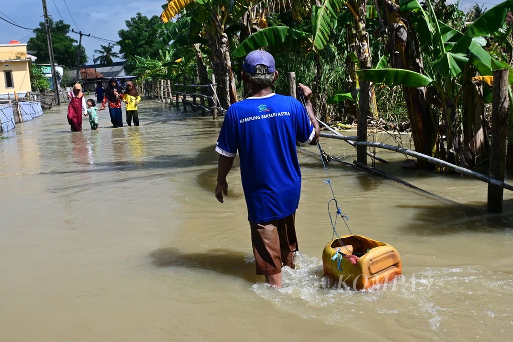 A number of residents walk on flooded streets in Pantai Harapan Jaya Village, Muara Gembong, on Friday (3/3/2023) afternoon. Floods have submerged this place since February 24, 2023.