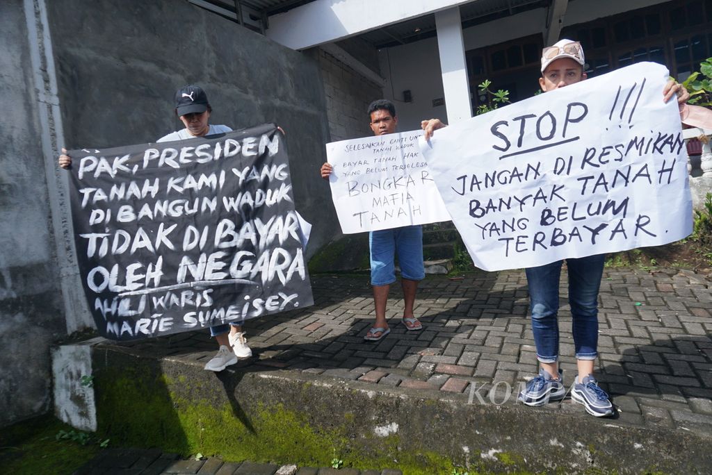Sendie Sumaraw (52, kiri) dan Debbie Sumaraw (51) membentangkan poster dan spanduk, Kamis (19/1/2023), untuk memprotes penyerobotan lahan seluas 4 hektar warisan orangtua mereka di Kecamatan Kalawat, Minahasa Utara, Sulawesi Utara. Lahan mereka kini telah menjadi bagian dari Bendungan Kuwil Kawangkoan yang diresmikan Presiden Joko Widodo pada hari yang sama.