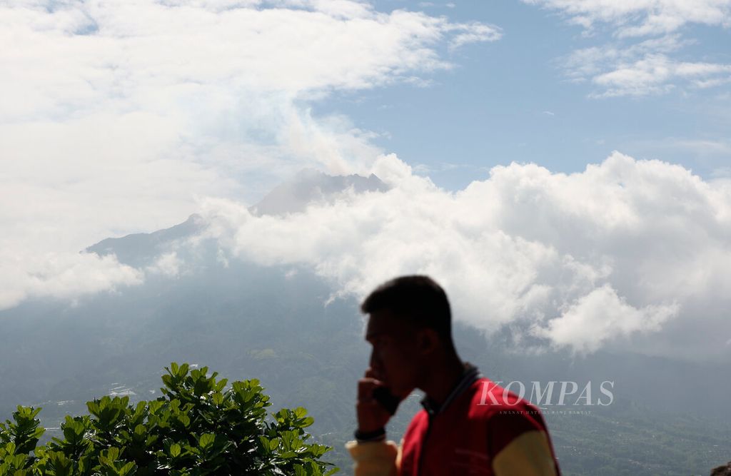Warga dengan latar belakang Gunung Merapi diselimuti awan tampak dari Ketep Pass, Kabupaten Magelang, Jawa Tengah, pada 13 Desember 2023.