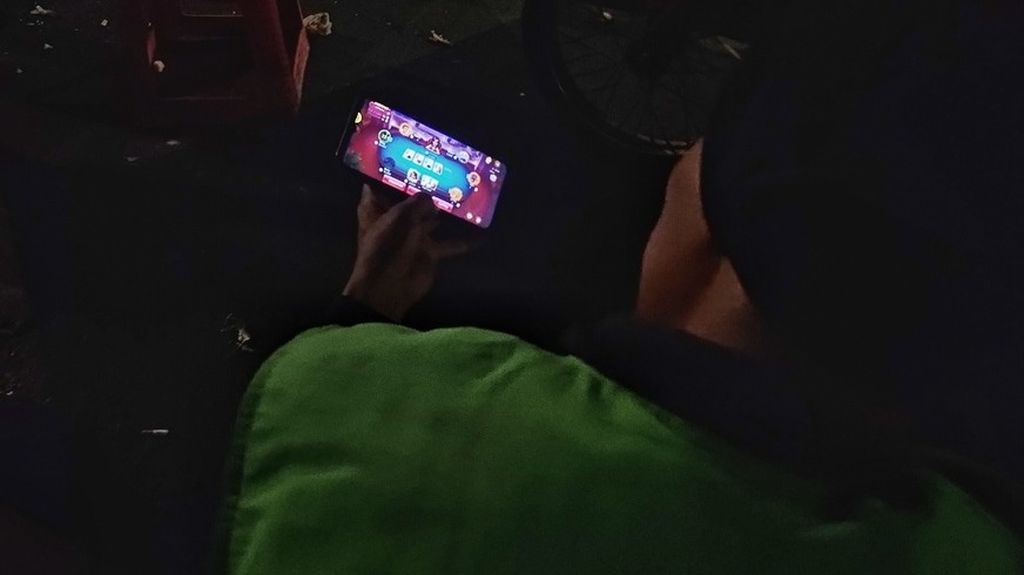 Seorang pengojek membuka situs judi poker dari ponsel di sekitar jembatan layang di Pancoran, Jakarta Selatan, Senin (20/11/2023).