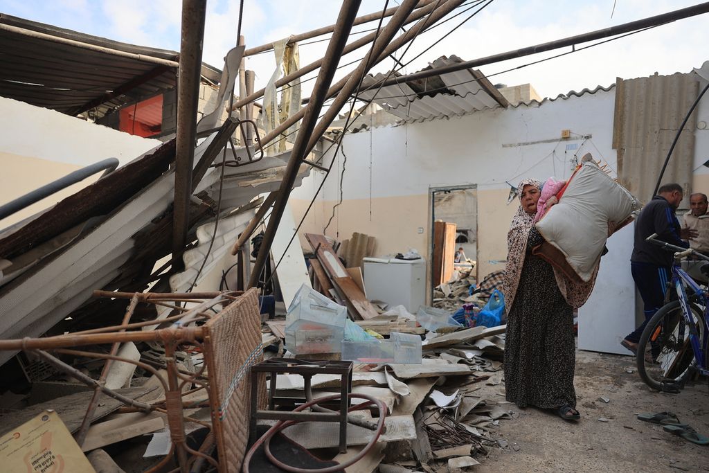 Seorang perempuan Palestina menyelamatkan barang-barang dari rumahnya yang rusak saat serangan udara Israel di Rafah, Jalur Gaza Selatan, Minggu (8/10/2023). 